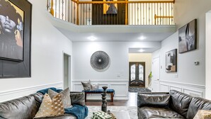 A spacious living room with leather sofas, a coffee table, and a staircase leading to a balcony. - Modern Stone Mountain Home w/ Spacious Deck, Grill (Stone Mountain)