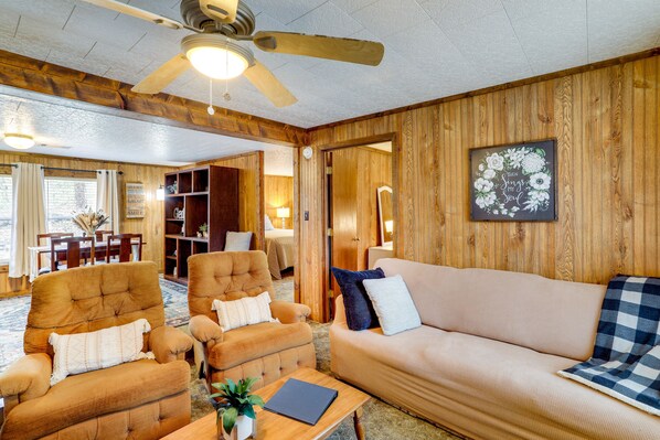 Une pièce chaleureuse avec un plafond en bois, un ventilateur de plafond, un canapé, deux fauteuils, une table basse avec une plante et un tableau encadré au mur.