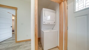 Un cuarto de lavado con lavadora y secadora apiladas, detalles de madera y una puerta que da a otra habitación.