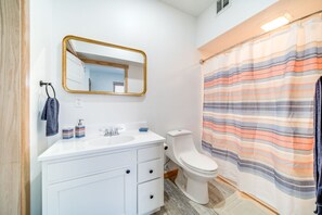 Et moderne badeværelse med et hvidt underskab, et spejl med gylden ramme, en stribet bruseforhæng og et hvidt toilet.