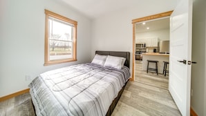 Un dormitorio con una cama grande, una ventana y una puerta abierta que da a una zona de cocina.
