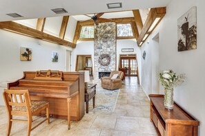 Un vaste espace de vie comprenant un piano, une cheminée, un pilier en pierre et une vue sur l’extérieur.