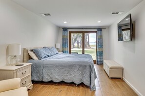Quarto com cama, mesas de cabeceira, um banco e televisão na parede.