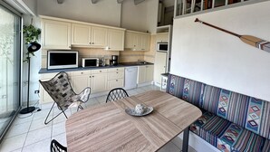 A modern kitchen with white cabinets, a dining table with chairs, and a patterned bench. - Appartement Front de Mer, Pleine Vue Mer, 5 Per, Wifi, Piscine, Animaux Acceptés (Agde)