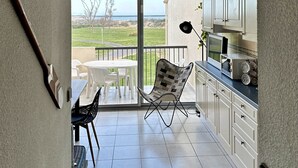 A modern kitchen with white cabinets, a dining area with a table and chairs, and a view of the outdoors. - Appartement Front de Mer, Pleine Vue Mer, 5 Per, Wifi, Piscine, Animaux Acceptés (Agde)