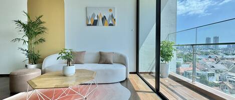 Un salon moderne avec un canapé blanc, une table basse aux motifs géométriques et deux plantes en pot. Un tableau représentant des montagnes et des oiseaux est accroché au mur.