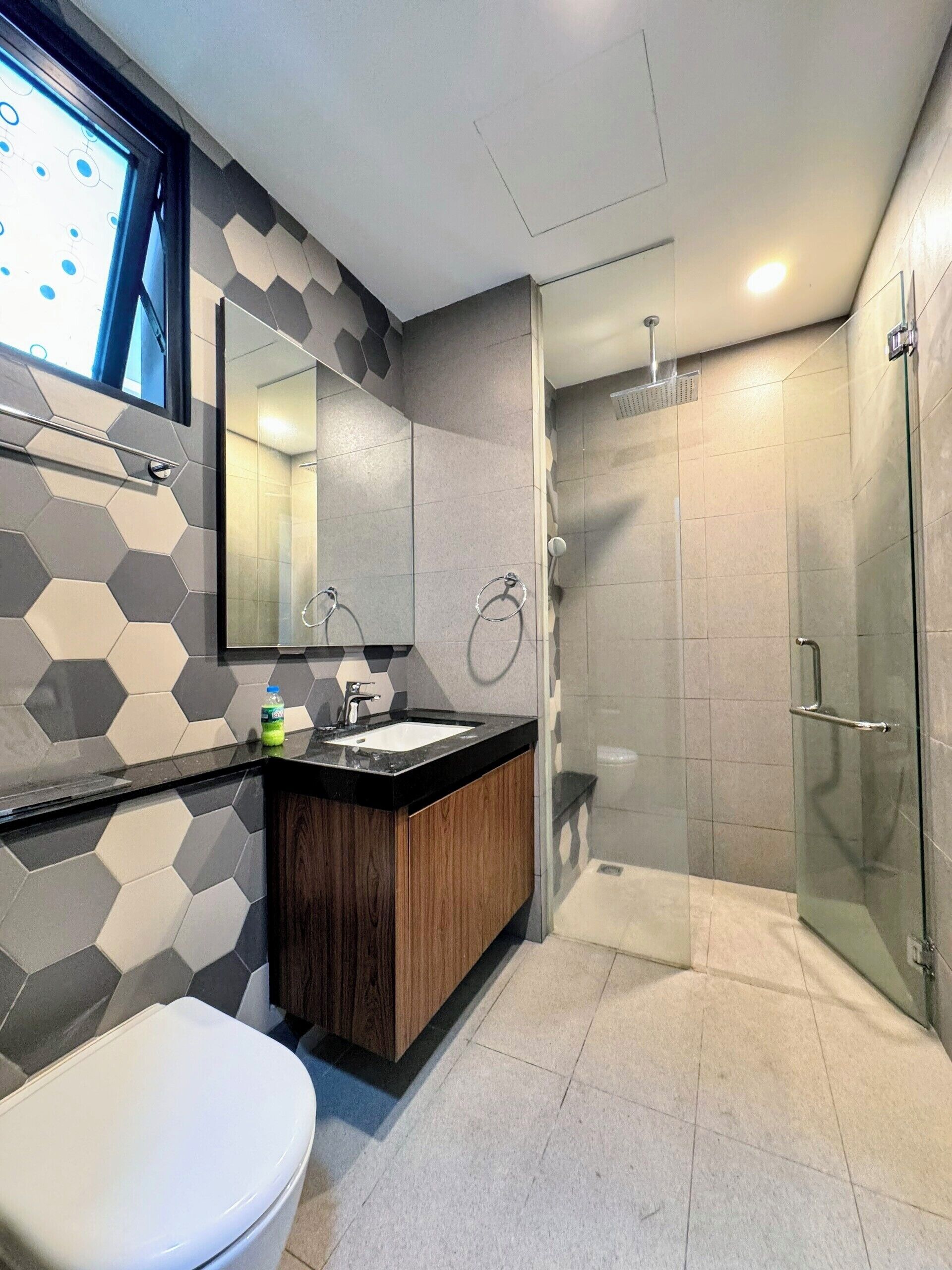 A modern bathroom with a hexagonal tile backsplash, a wooden vanity, a white toilet, and a glass-enclosed shower.