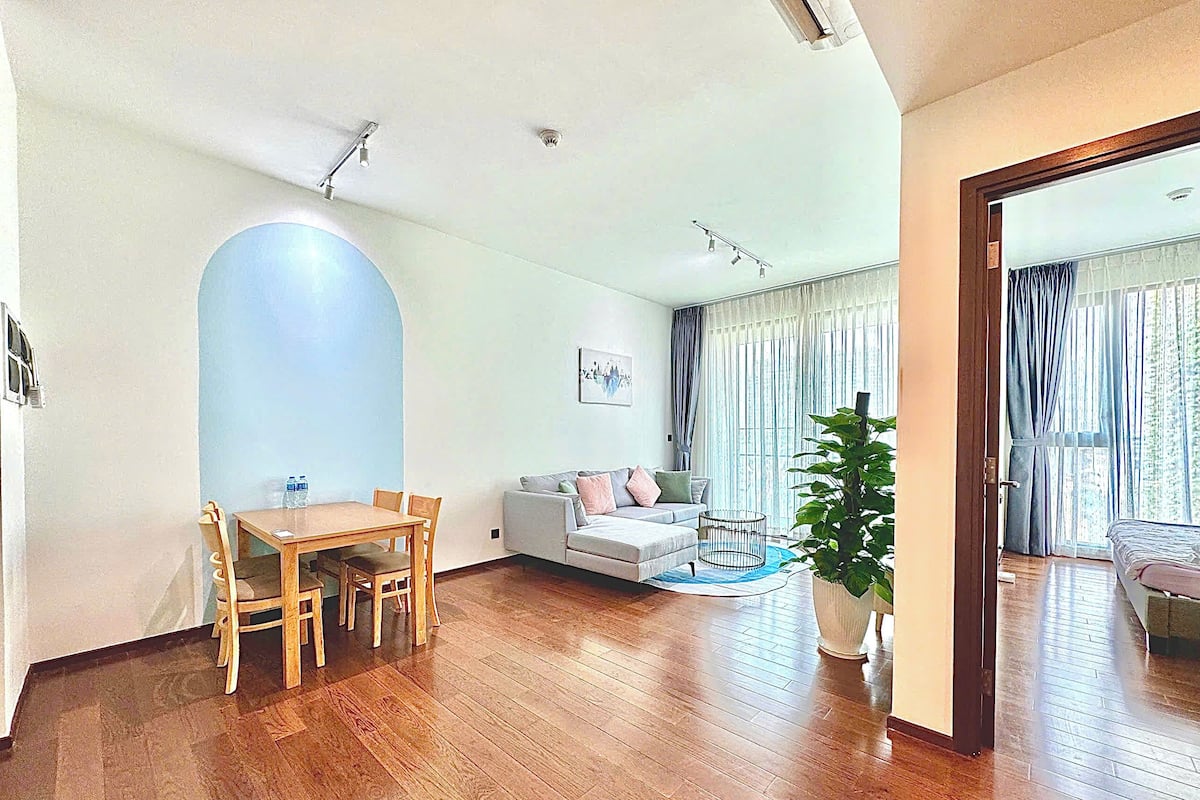 A spacious living room with a wooden dining table, a sofa, and a large potted plant.