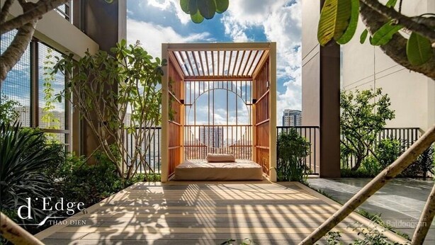Un espace extérieur moderne, aménagé avec un coin salon et une pergola en bois, entouré d’une végétation luxuriante et doté de grandes fenêtres offrant une vue sur le paysage urbain.