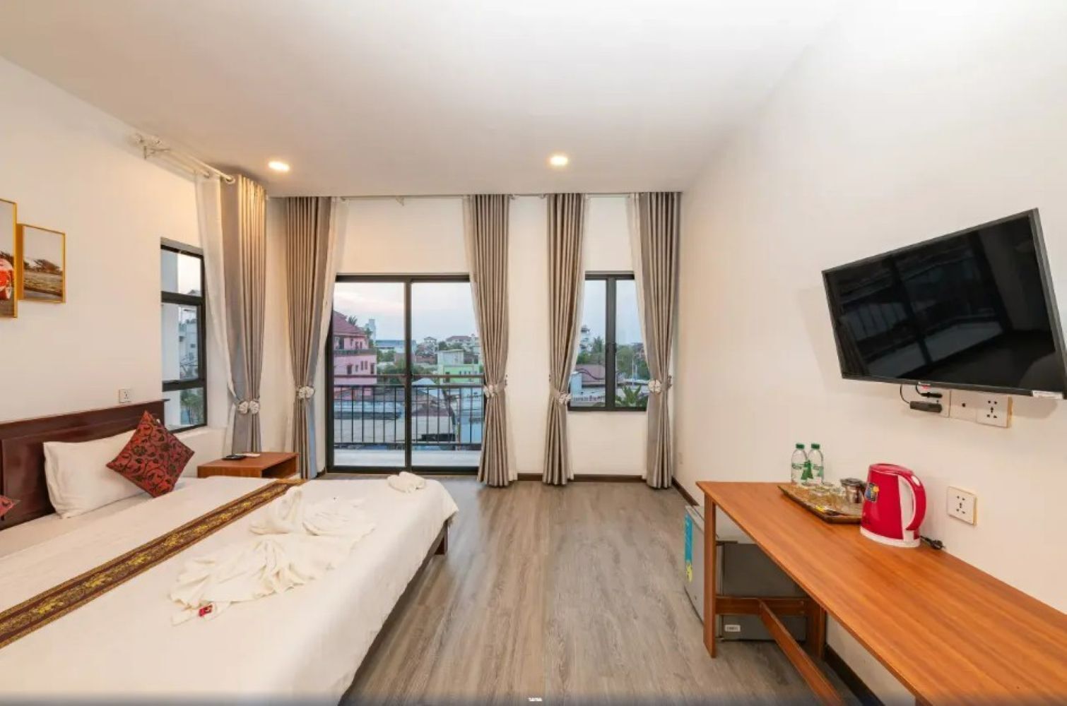 A hotel room with a bed, a desk, a TV, and a balcony with curtains.