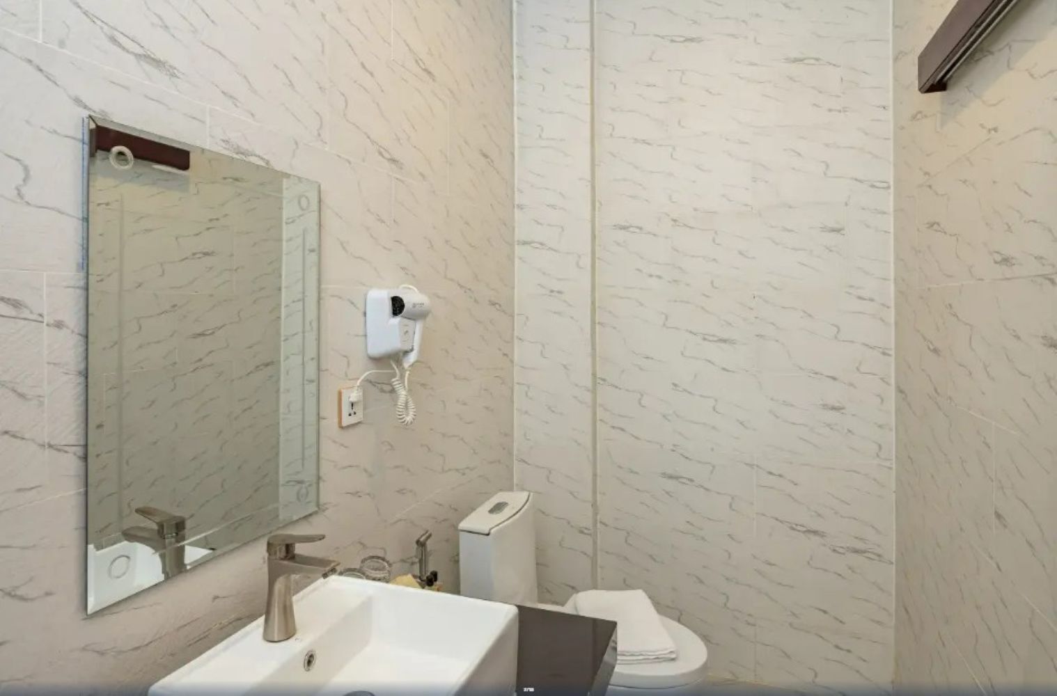 A bathroom with a marble wall, a sink, a toilet, and a mirror.