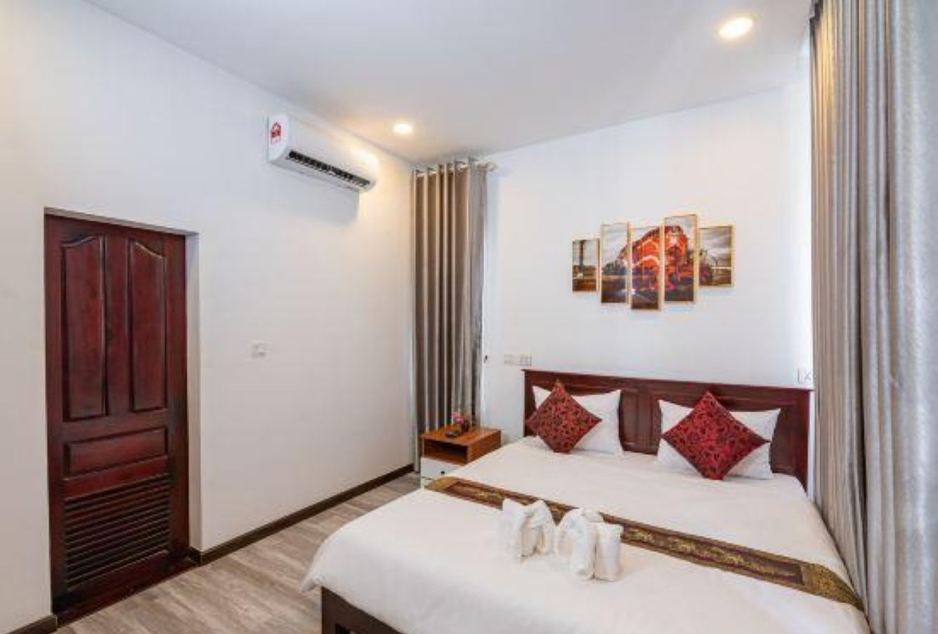 A hotel room with a large bed, a wooden door, an air conditioning unit, and a nightstand with a lamp.