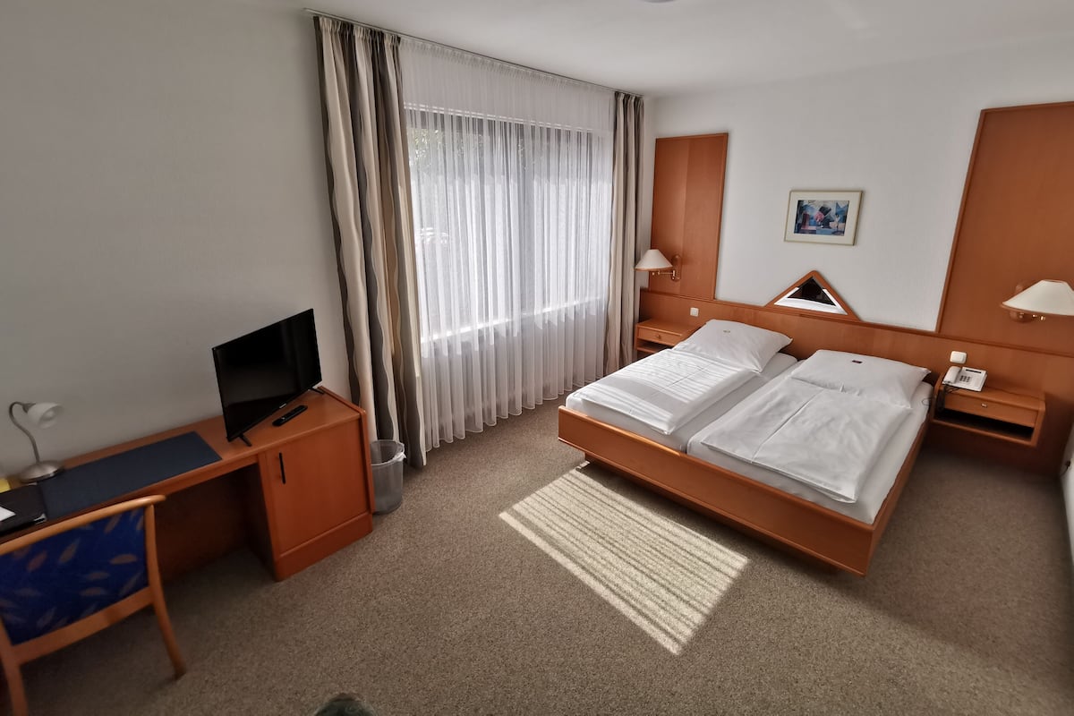 A hotel room with a bed, desk, TV, and a window with curtains.