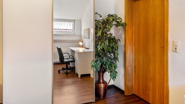 Une pièce avec un plancher en bois, un bureau avec une chaise, une plante en pot et une porte en bois.