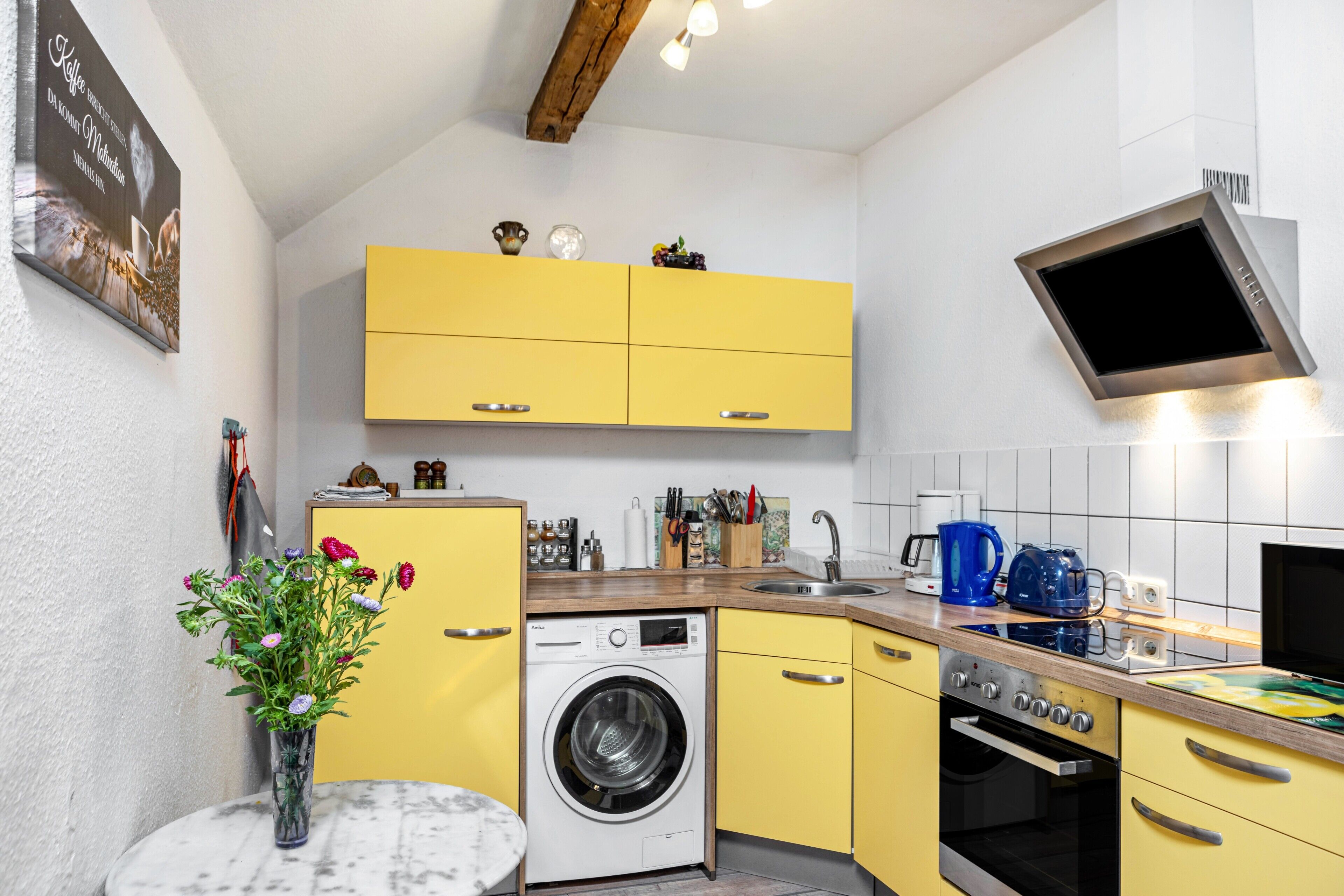 A compact kitchen with yellow cabinets, a washing machine, an oven, and a sink.