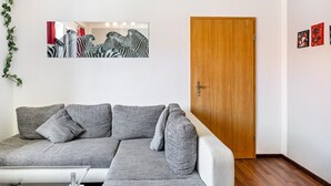 Un salon avec un canapé gris, une porte en bois et un miroir orné d’une œuvre d’art représentant un zèbre.