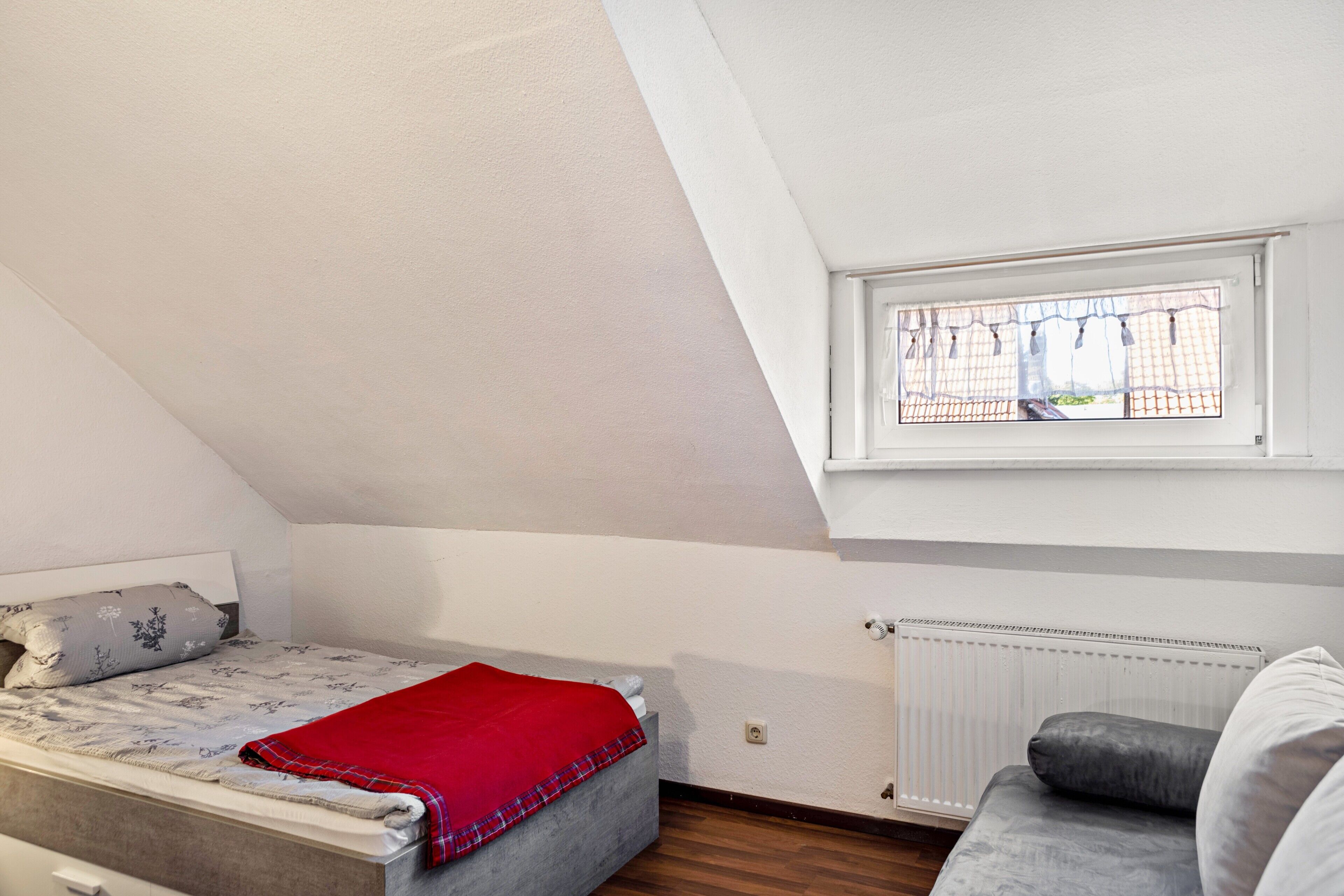 Ein Schlafzimmer mit Bett, Fenster, Heizkörper und einer Couch.