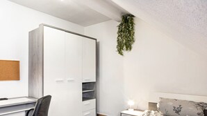 Une chambre à coucher comprenant un lit, un bureau, une chaise, une armoire et une plante suspendue.