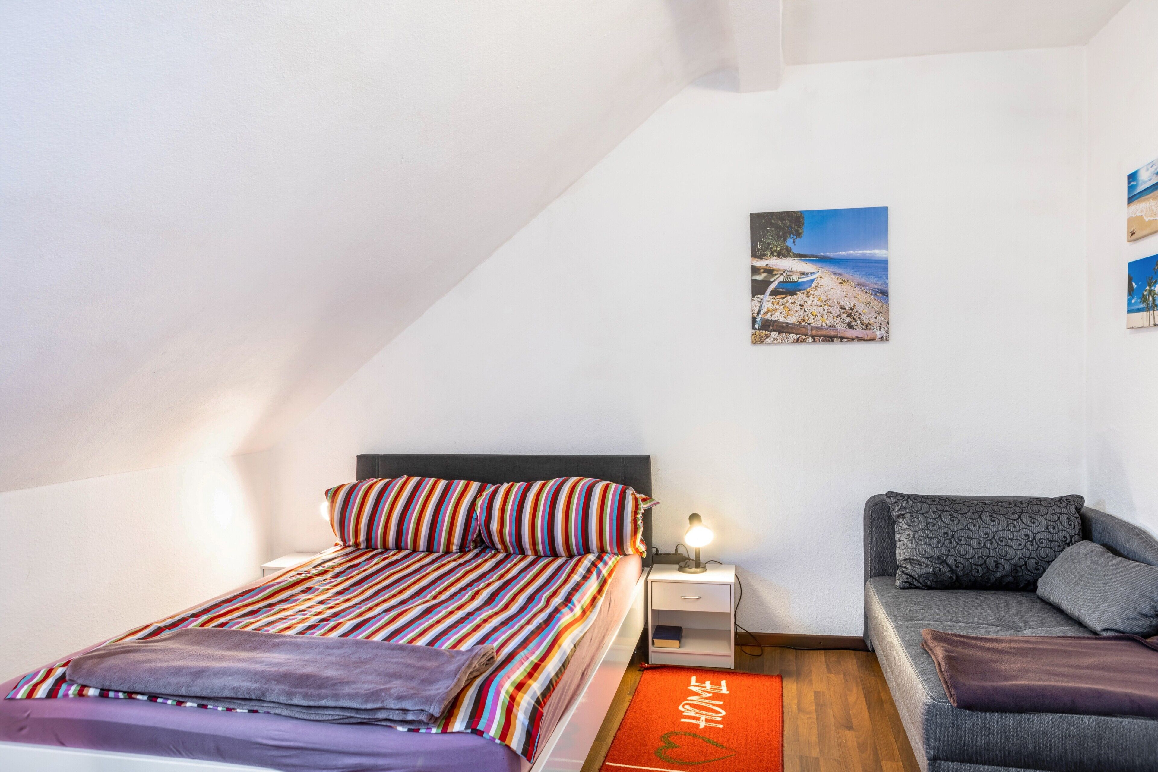 A bedroom with a bed, a sofa, a nightstand, a lamp, and a picture on the wall.