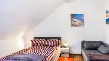 A bedroom with a bed, a sofa, a nightstand, a lamp, and a picture on the wall.