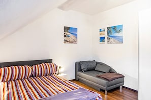 A bedroom with a bed, a sofa, and two wall-mounted pictures of beaches. - Apartment 'Thüringer Wald' with Wi-Fi (Ilmenau)