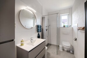 Une salle de bain moderne avec un miroir rond, un lavabo, une douche et des toilettes.