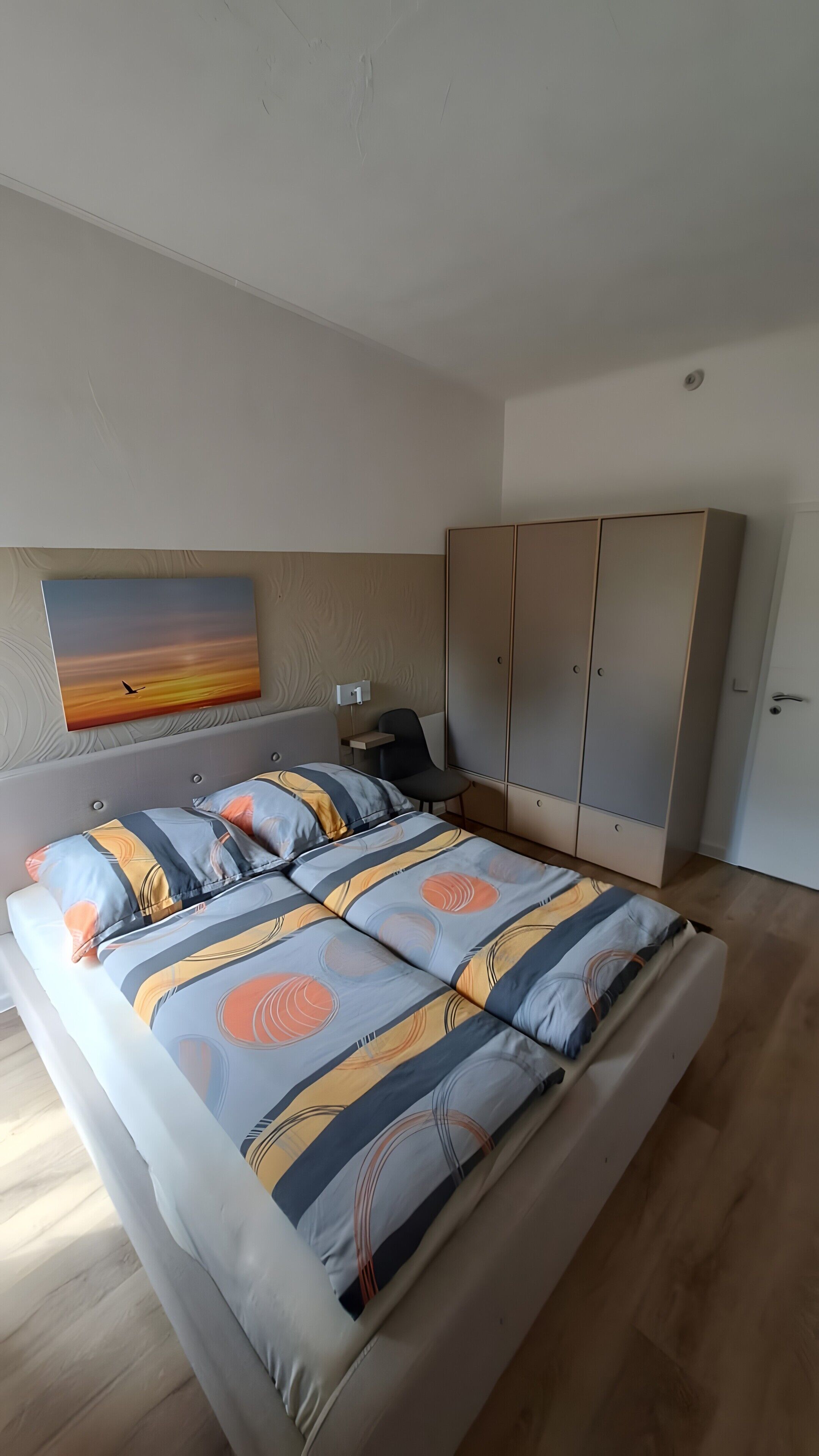 Une chambre à coucher avec un lit, une chaise, une armoire et un tableau accroché au mur.