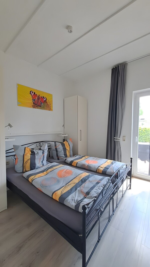 Un dormitorio con una cama, un armario, un cuadro y vistas por la ventana.