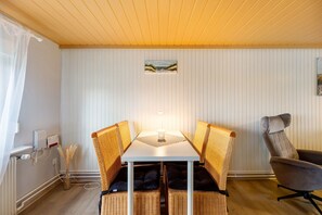 A dining area with a white table, wicker chairs, a grey armchair, and a wall-mounted painting.