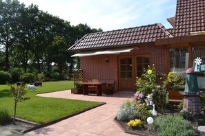 Ein Ziegelhaus mit einem Ziegeldach, eine Terrasse mit Tisch und Stühlen sowie ein Garten mit verschiedenen Pflanzen und einer Windmühle.