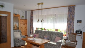 A living room with a sofa, armchairs, a wooden coffee table, a dining table, and a window with curtains.