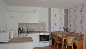 A compact kitchen with a microwave, coffee maker, and oven. There is a dining area with a wooden table and two chairs.