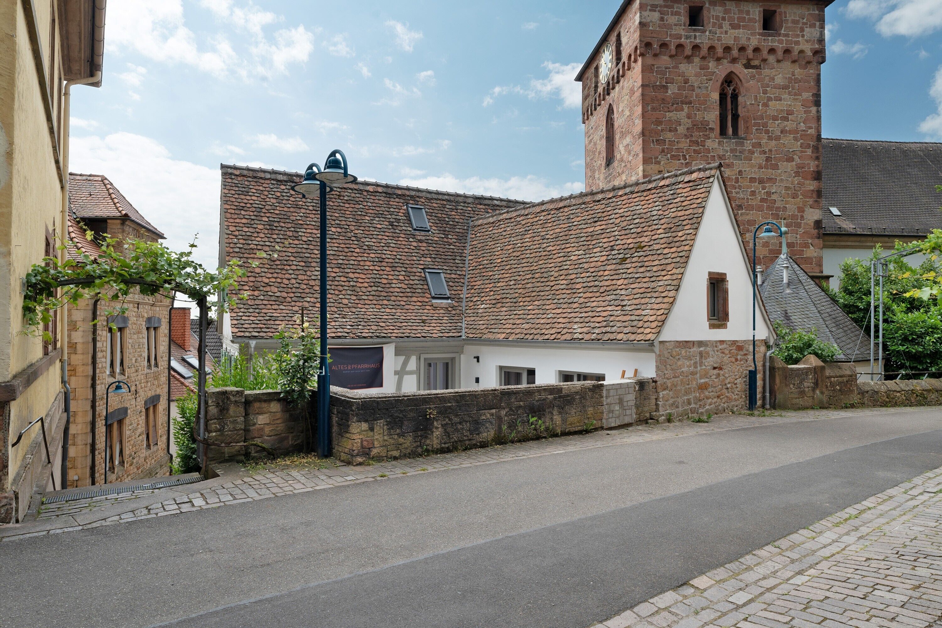 A street with a historic building featuring a tower, a white building with a sloped roof, and a paved road.