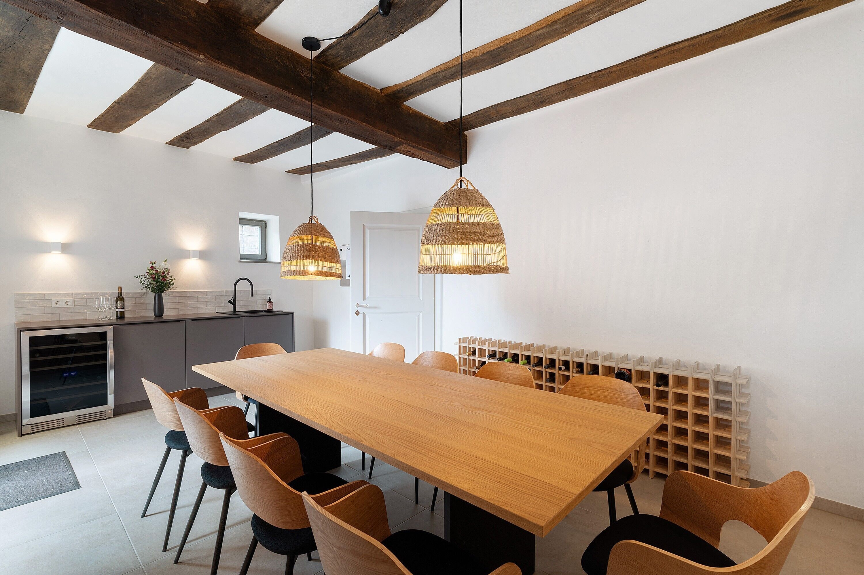 Una cocina moderna con una mesa y sillas de madera, luces colgantes y una estantería empotrada para vinos.