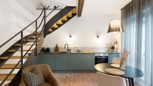 Una cocina moderna con piso de patrón tipo espiga, un comedor con mesa redonda y sillas, y una escalera con barandilla negra.