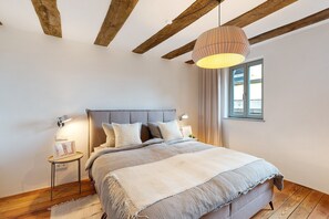 A bedroom with a bed, bedside lamps, a window, and exposed wooden beams. - Apartment "Altes Pfarrhaus - Studio" with Shared Terrace & Wi-Fi (Gleisweiler)