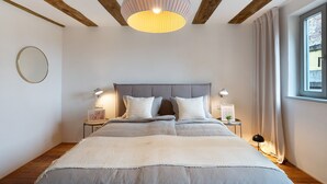 Un dormitorio con cama, lámparas de noche, un espejo redondo y una ventana con cortinas.
