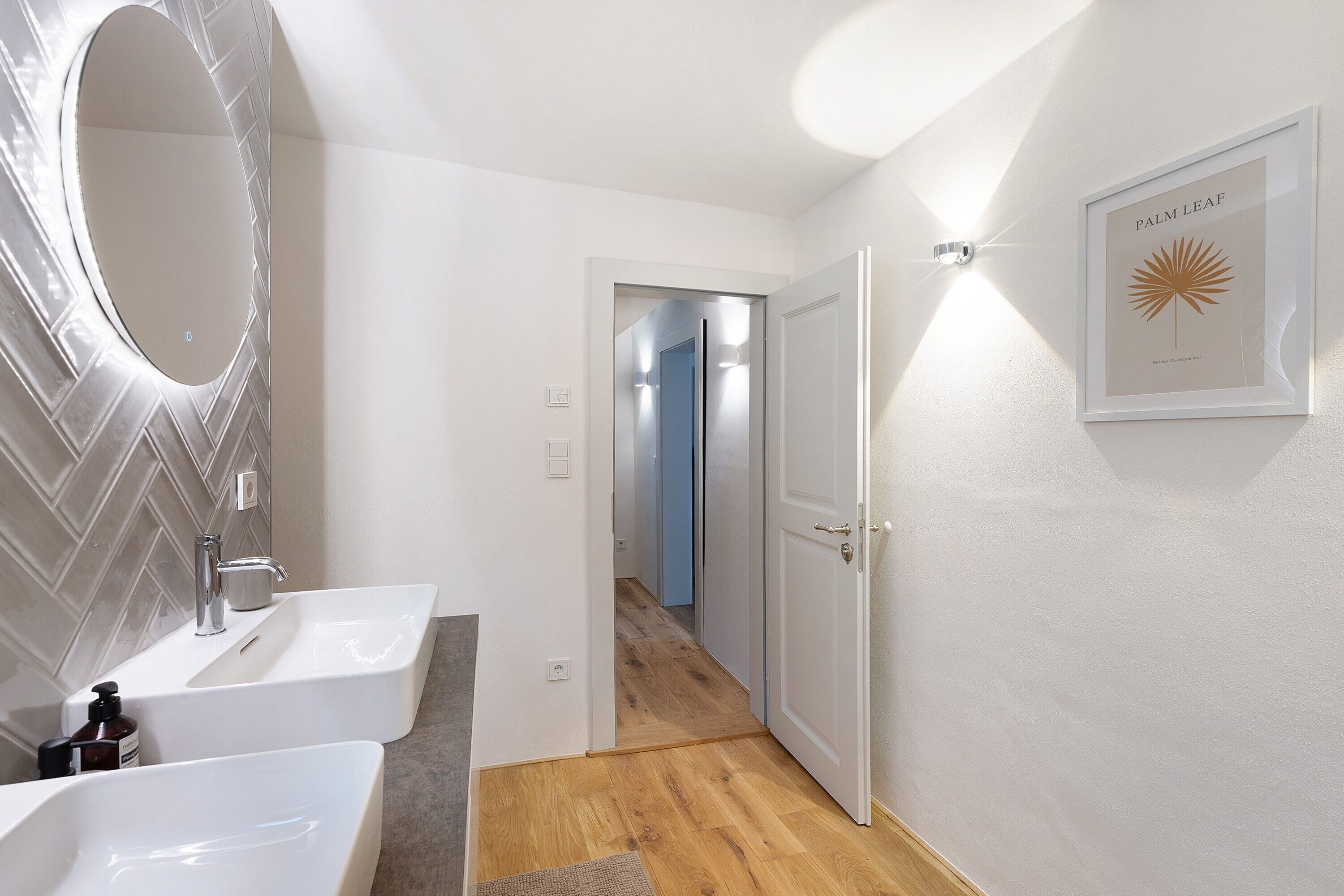 Ein modernes Badezimmer mit zwei Waschbecken, einem großen Spiegel und einem gerahmten Kunstwerk an der Wand.