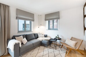 A modern living room with a grey sectional sofa, a small round table, a wicker chair, and a patterned rug. - Apartment "Altes Pfarrhaus - Studio" with Shared Terrace & Wi-Fi (Gleisweiler)