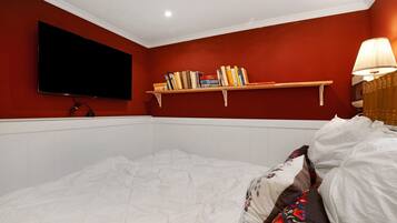 A bedroom with a bed, a mounted TV, a shelf with books, and a bedside lamp.