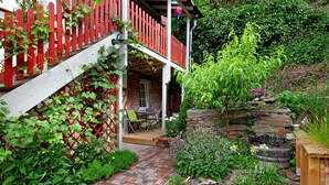 Um jardim com cerca vermelha, deck de madeira e parede de pedra.