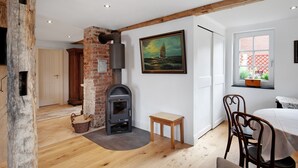 Um quarto com lareira, piso de madeira, mesa de jantar com cadeiras, um quadro na parede e uma janela com vista.