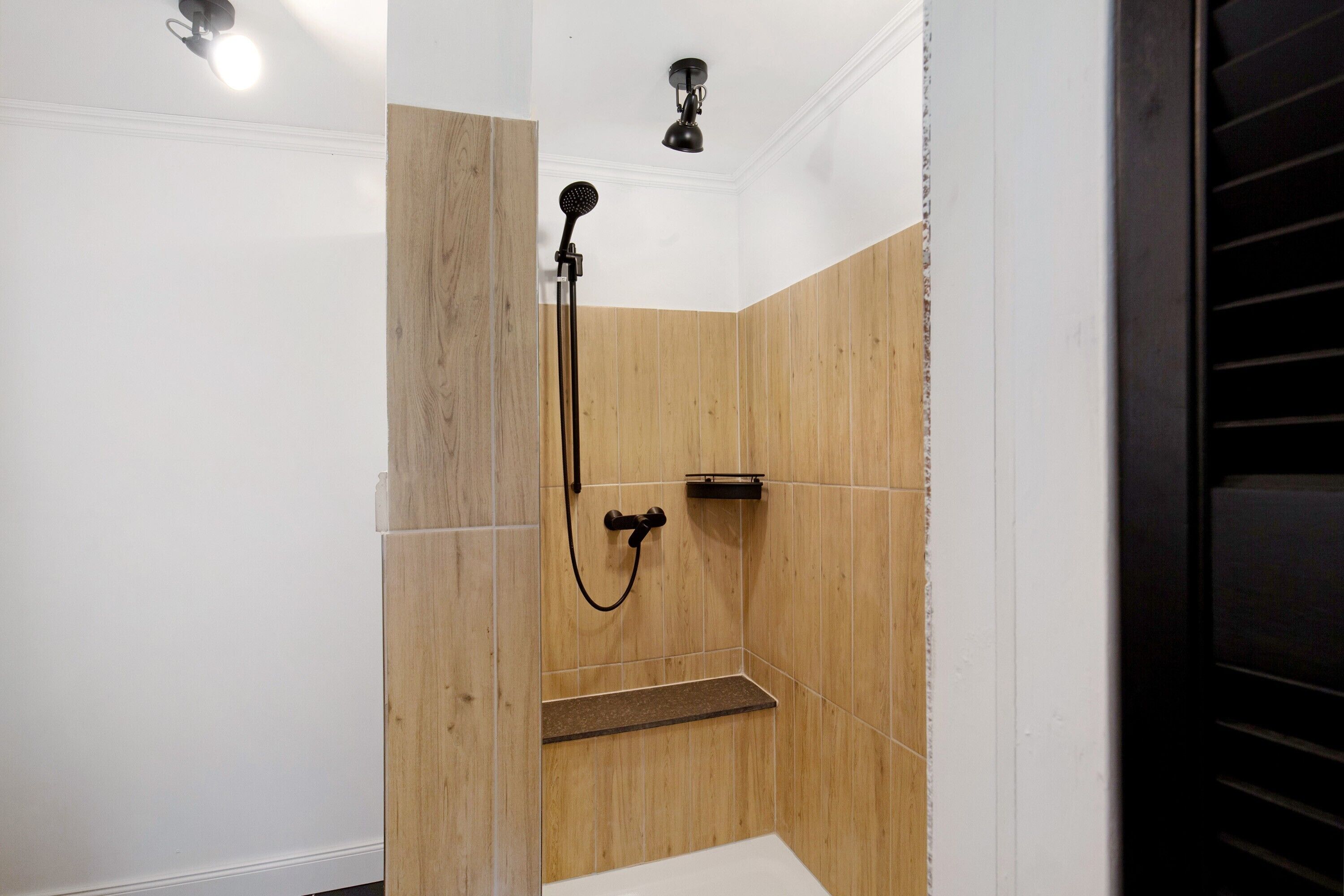 Douchegedeelte met houten lambrisering, een handdouche en een wandmengkraan.