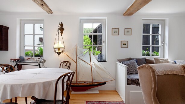Uma área de refeições com um modelo de barco à vela, cadeiras de madeira, uma mesa e um lustre.