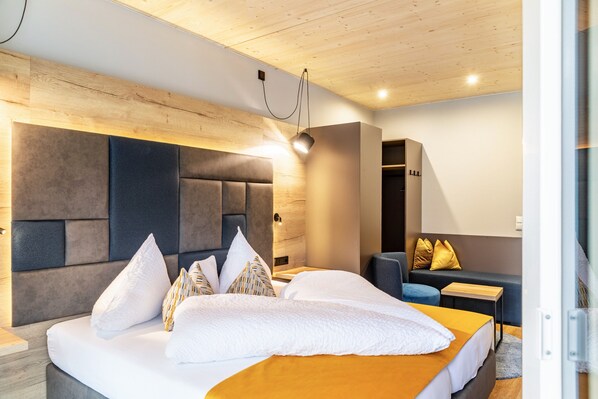 A modern hotel room with a large bed, a sofa, a small table, and a wooden ceiling.