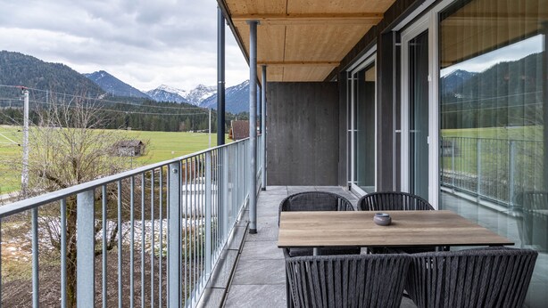 Un balcon doté d’un plafond en bois, une table avec des chaises et une vue sur les montagnes.
