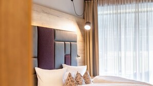Une chambre d’hôtel moderne avec une tête de lit en bois, une grande fenêtre avec des rideaux légers et une lampe de chevet.