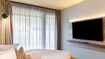 A modern hotel room with a large bed, a television mounted on the wall, and a window with sheer curtains.