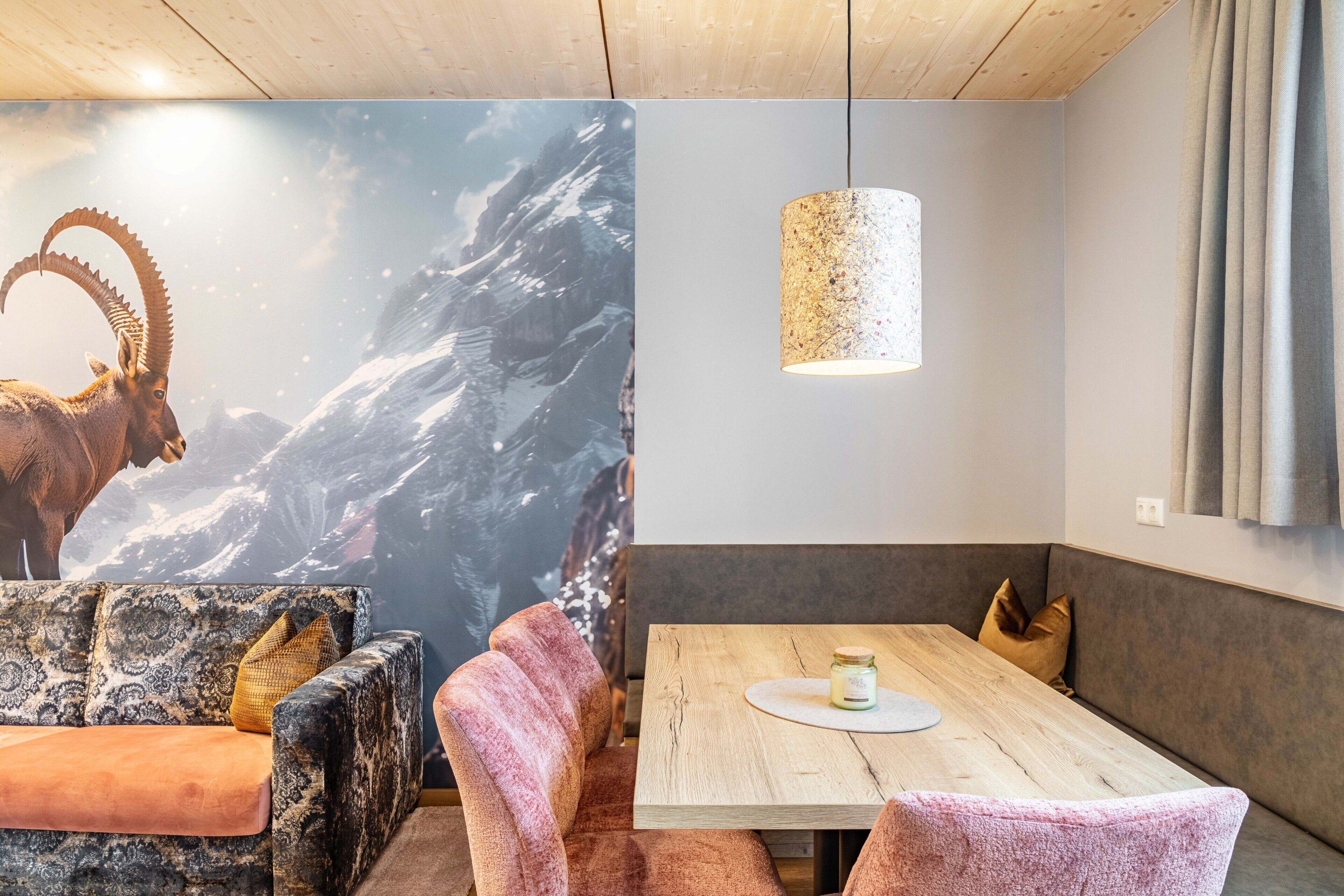 Une pièce décorée d’une fresque représentant une montagne, une table en bois avec une bougie et des fauteuils confortables.