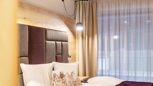 Ein modernes Hotelzimmer mit einem Holzkopfteil, einem großen Bett mit vielen Kissen, einem Nachttisch und einem Fenster mit durchscheinenden Vorhängen.